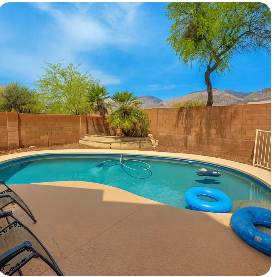 Curved backyard swimming pool with blue inflatable rings, desert landscaping, and mountains in the distance.