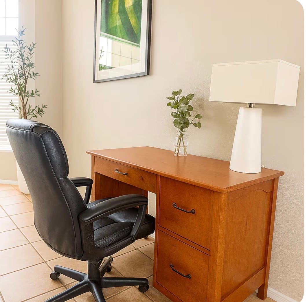 Wooden desk with a white lamp, small plant, and a black leather office chair.